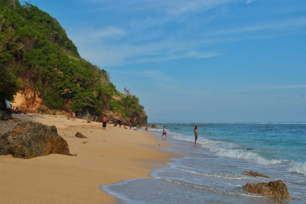 Der Gunung Payung Beach ist ein kleines Stück Strand vor der Steilküste. Die Sonne geht langsam unter, Besucher genießen den Ort.