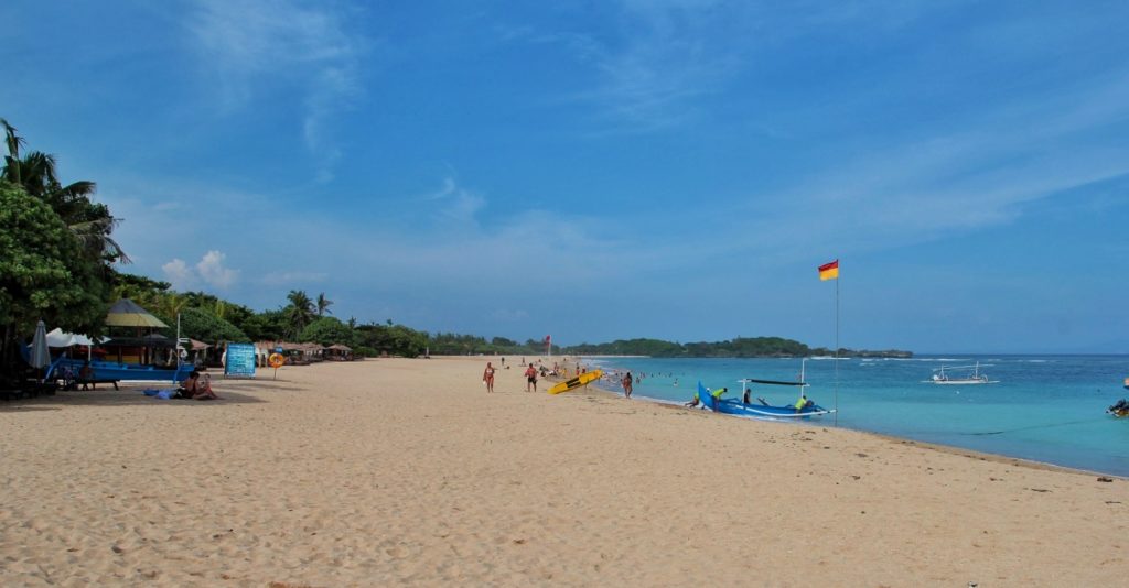 Der Nusa Dua Beach mit Fahne, Boot und ein paar Menschen, die am Strand entlanglaufen
